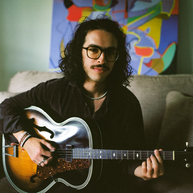 Jordi posed with his guitar against an abstract background.