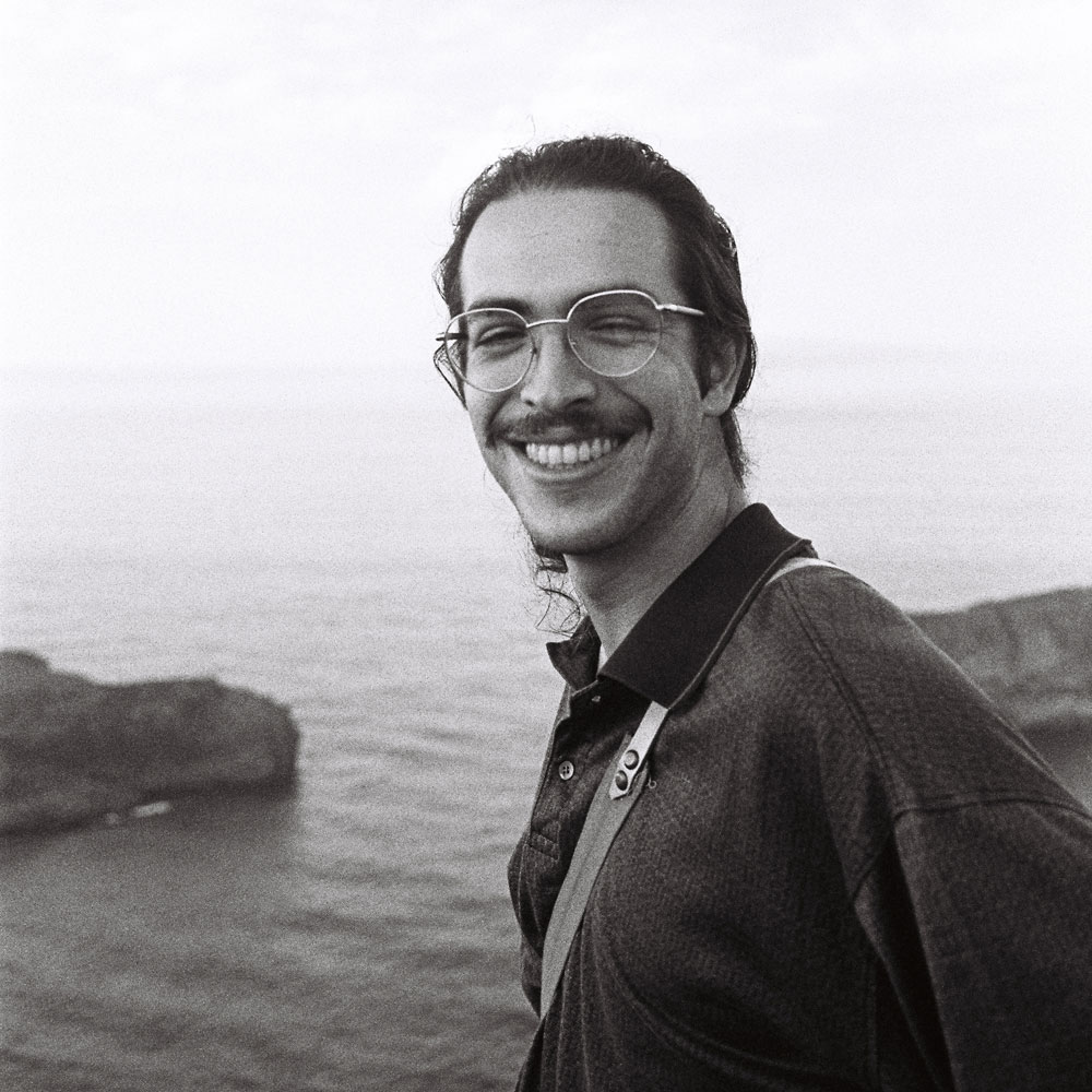 Jordi gives a big smile to the camera in front of the ocean.