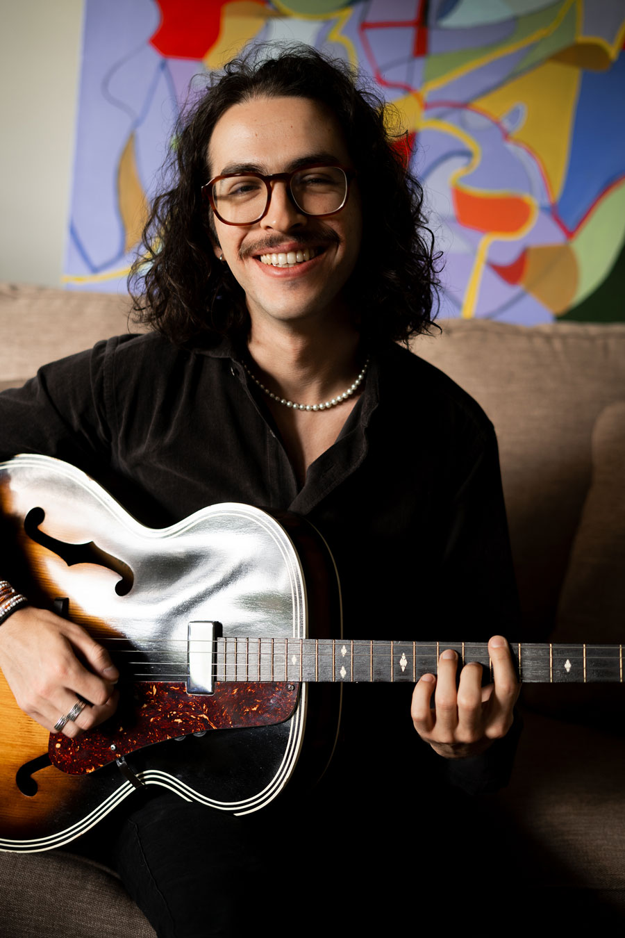 Jordi smiles posed with his guitar against an abstract background.