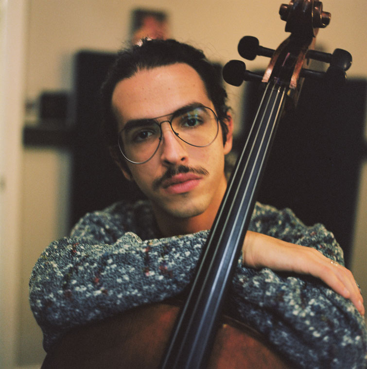 With his arms resting atop his cello, Jordi gives the camera a look of sincerity.