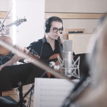 Jordi playing the cello with a full orchestra as part of a live studio recording session.